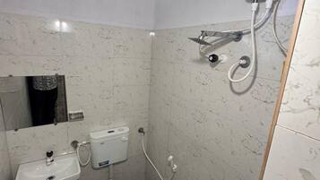 Un baño con inodoro, lavamanos y cabezal de ducha manual instalado en la pared.