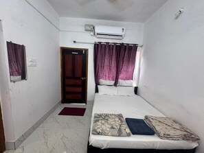 A bedroom with a bed, an air conditioner, a door, and a window with curtains. - Silver Sand Beach Homestay (Bhatkal)
