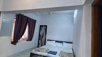 Un dormitorio con cama, una mesa, un ventanal con cortinas y un ventilador de techo.