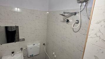 Un baño con inodoro, lavabo y cabezal de ducha de mano instalado en la pared.