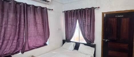 A bedroom with a bed, curtains, a ceiling fan, an air conditioning unit, and a wooden door.