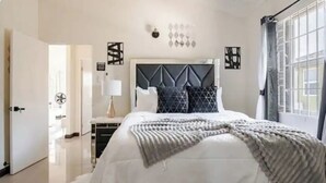 Un dormitorio con cama, mesita de noche, lámpara y ventana con cortinas.