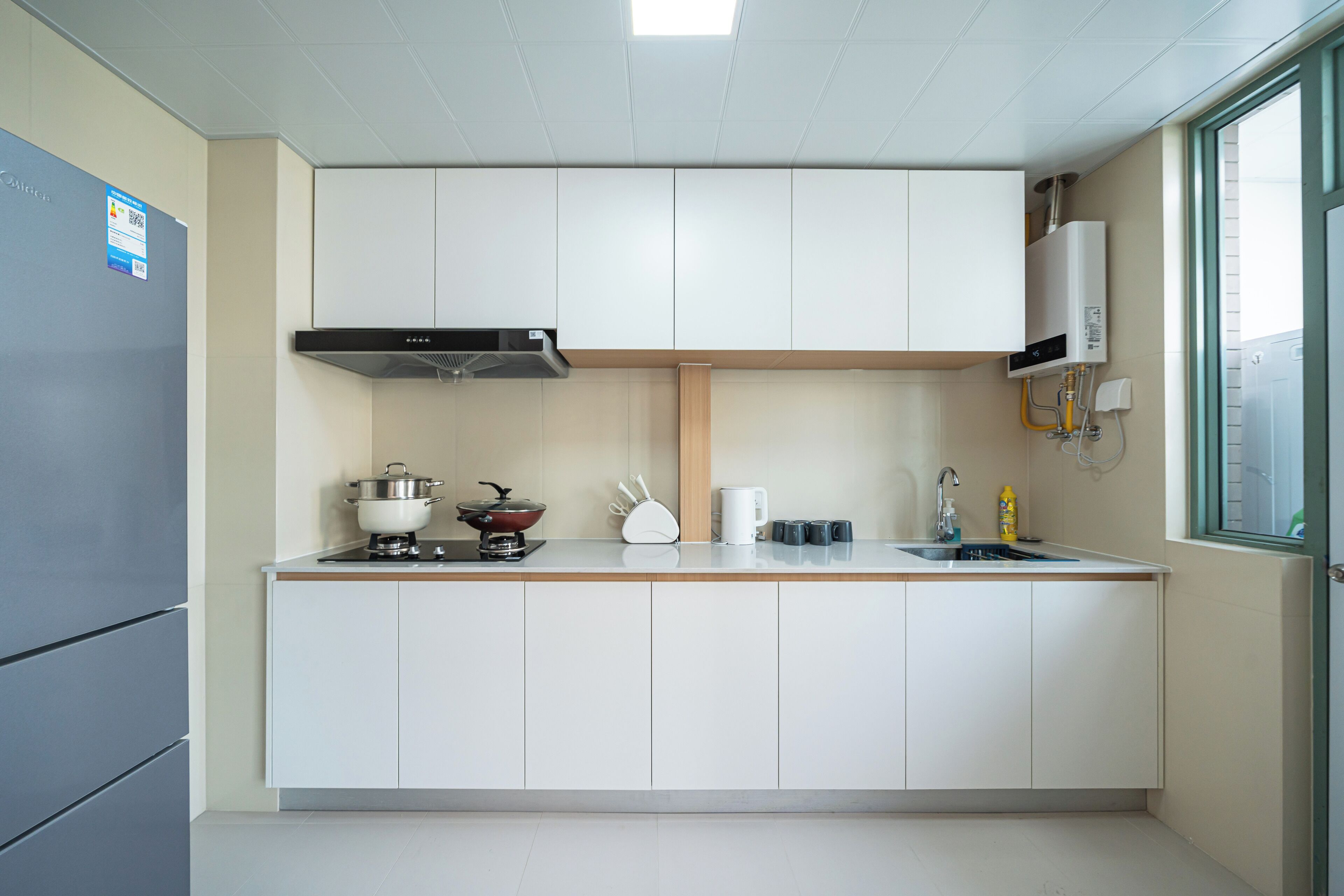 A modern kitchen with white cabinets, a stove, a kettle, and a microwave.