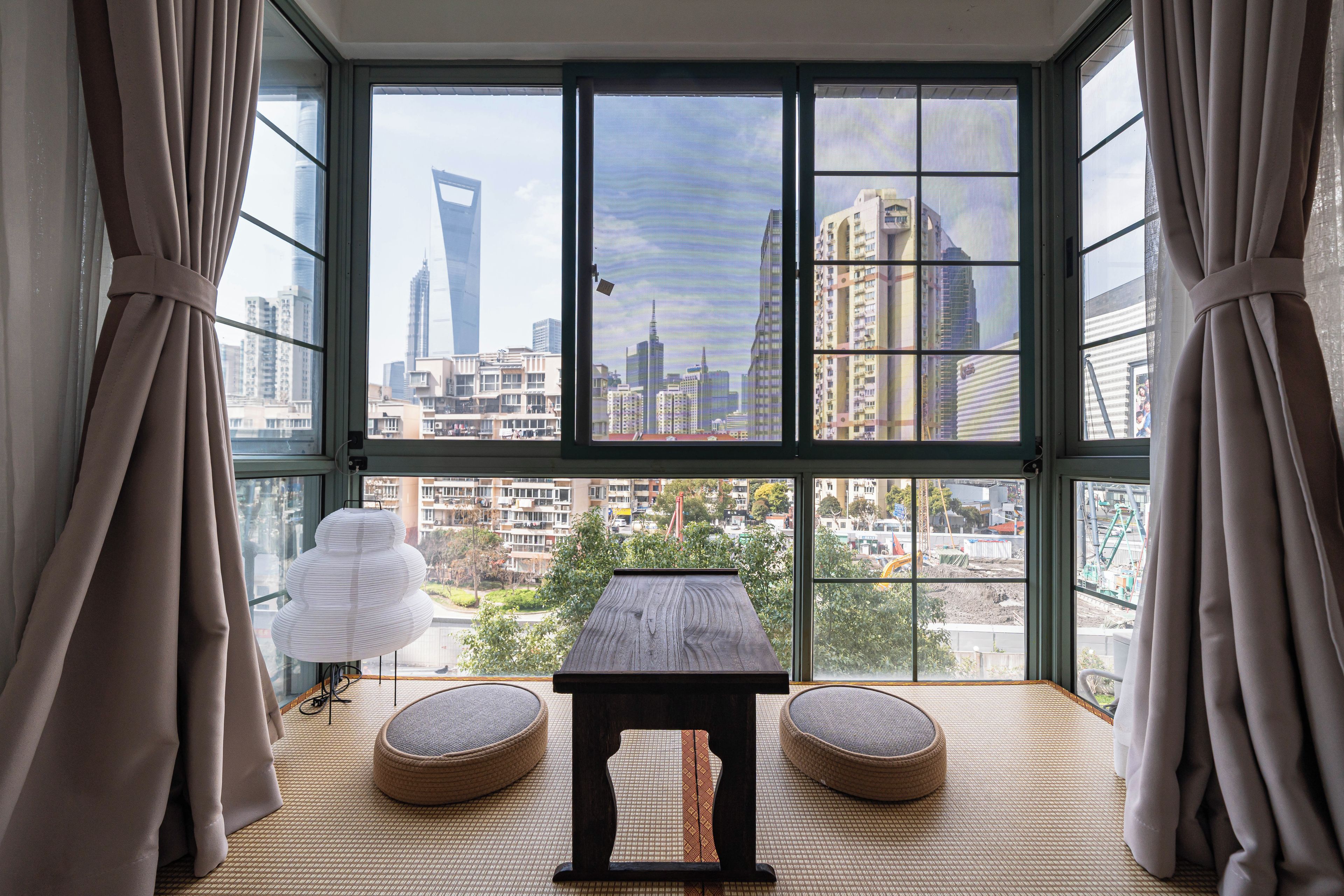A room with a large window, a table, two cushioned seating areas, and a decorative lamp.
