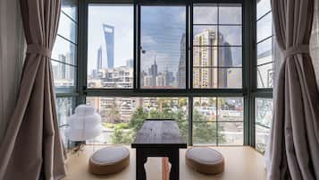 A room with a large window, a table, two cushioned seating areas, and a decorative lamp.