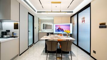 A modern kitchen with a dining area, equipped with a large flat-screen TV, a coffee machine, and a water dispenser.