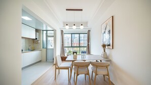 A modern kitchen with white cabinets, a dining area with a wooden table and chairs, and a large window with curtains. - Today Aparthotel (Shanghai)