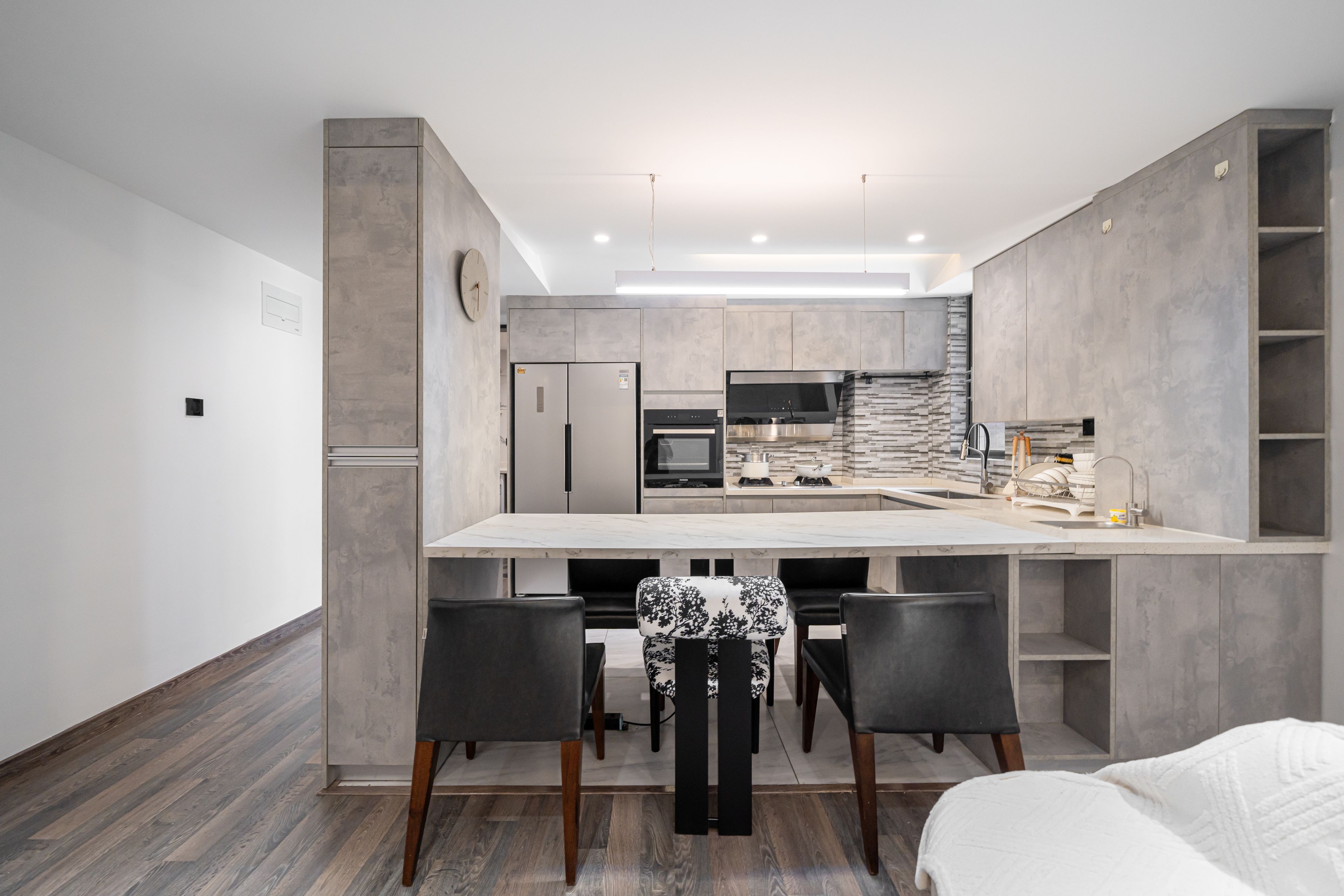 A modern kitchen with a central island, dark chairs, and a dining table.