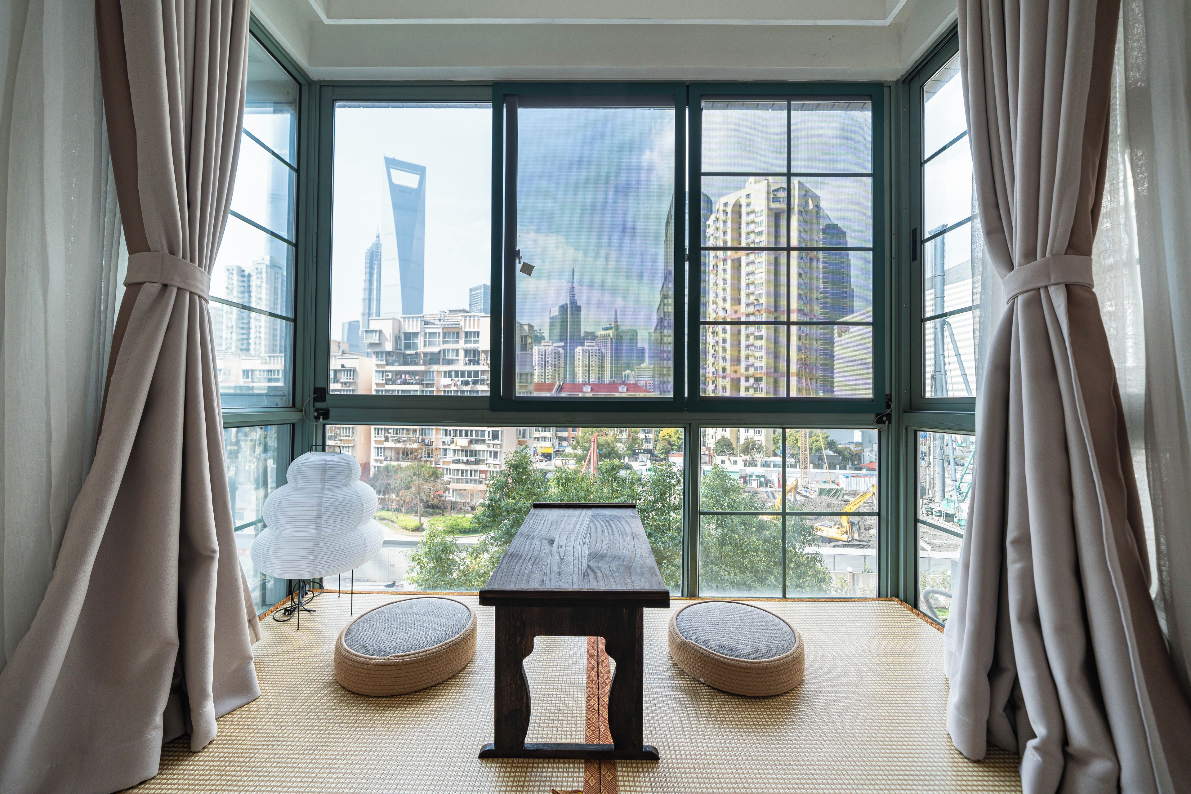 A room with a large window, a table, and two round seating areas.