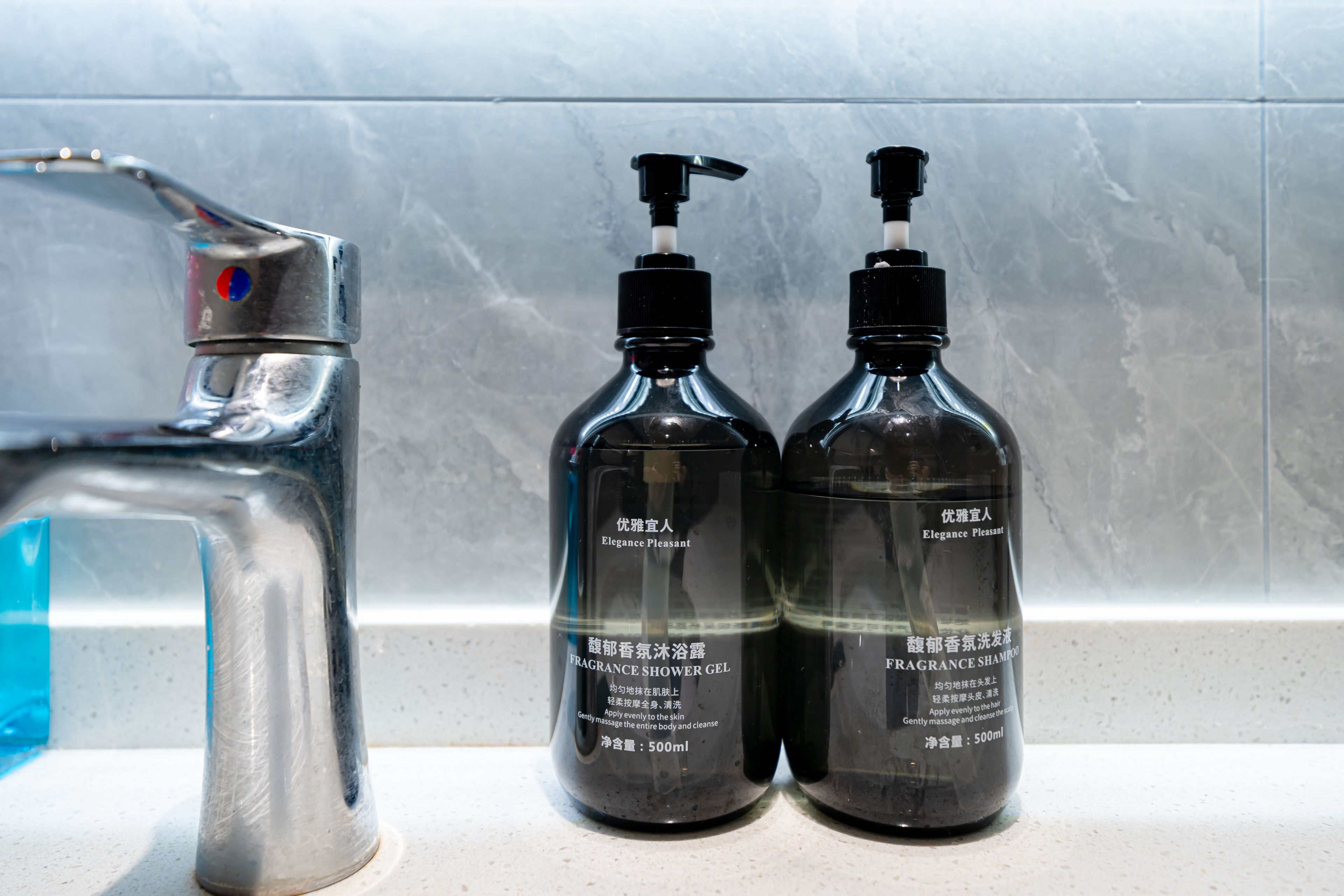 Two black bottles with pumps and a silver faucet on a countertop.