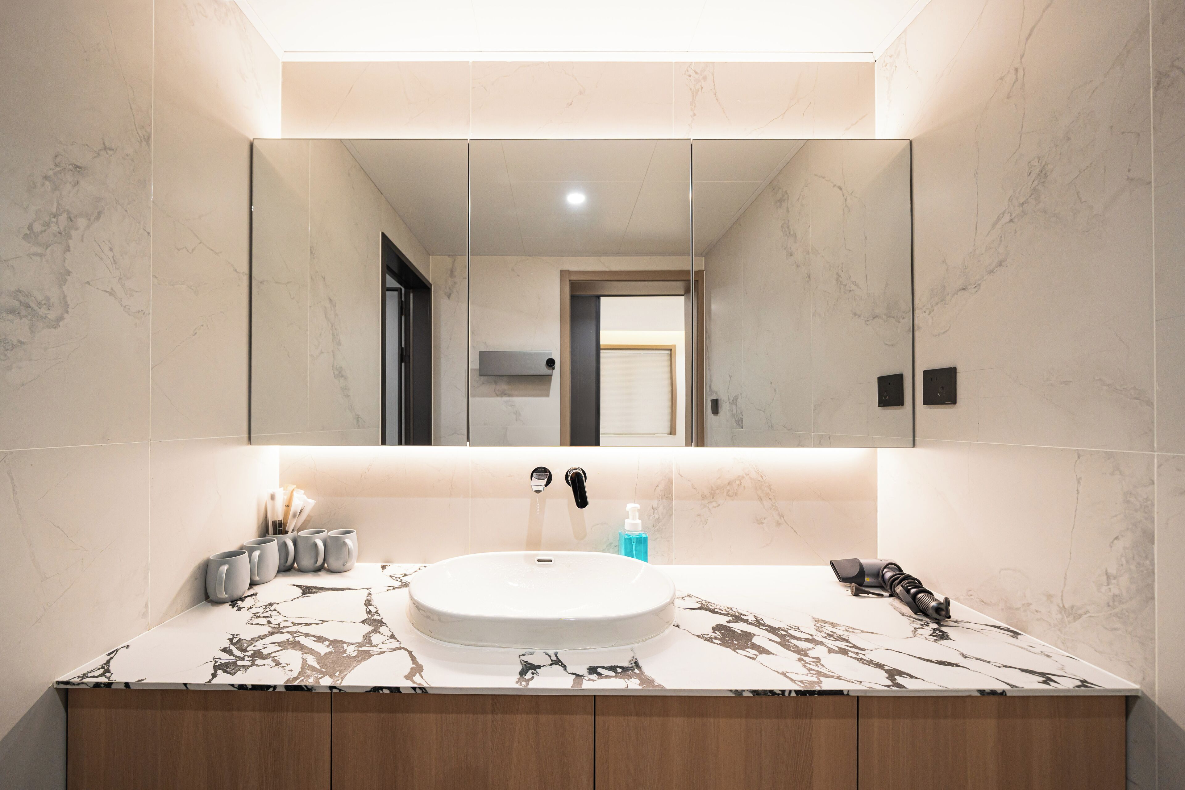 Un baño moderno con lavamanos de mármol, un espejo grande y muebles de madera.