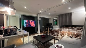 Una habitación de hotel moderna con una cama, un escritorio con ordenador, un televisor y un área de comedor.