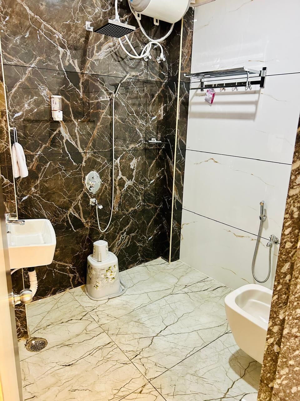 A bathroom with a marble floor, a white sink, a toilet, a shower area with a handheld showerhead, and a towel rack.