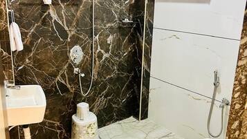 A bathroom with a marble floor, a white sink, a toilet, a shower area with a handheld showerhead, and a towel rack.