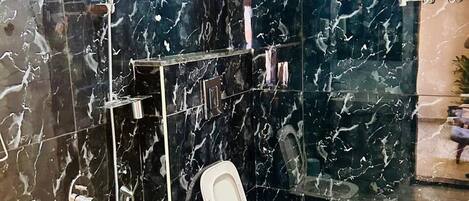 A bathroom with a shower, toilet, and a marble wall.