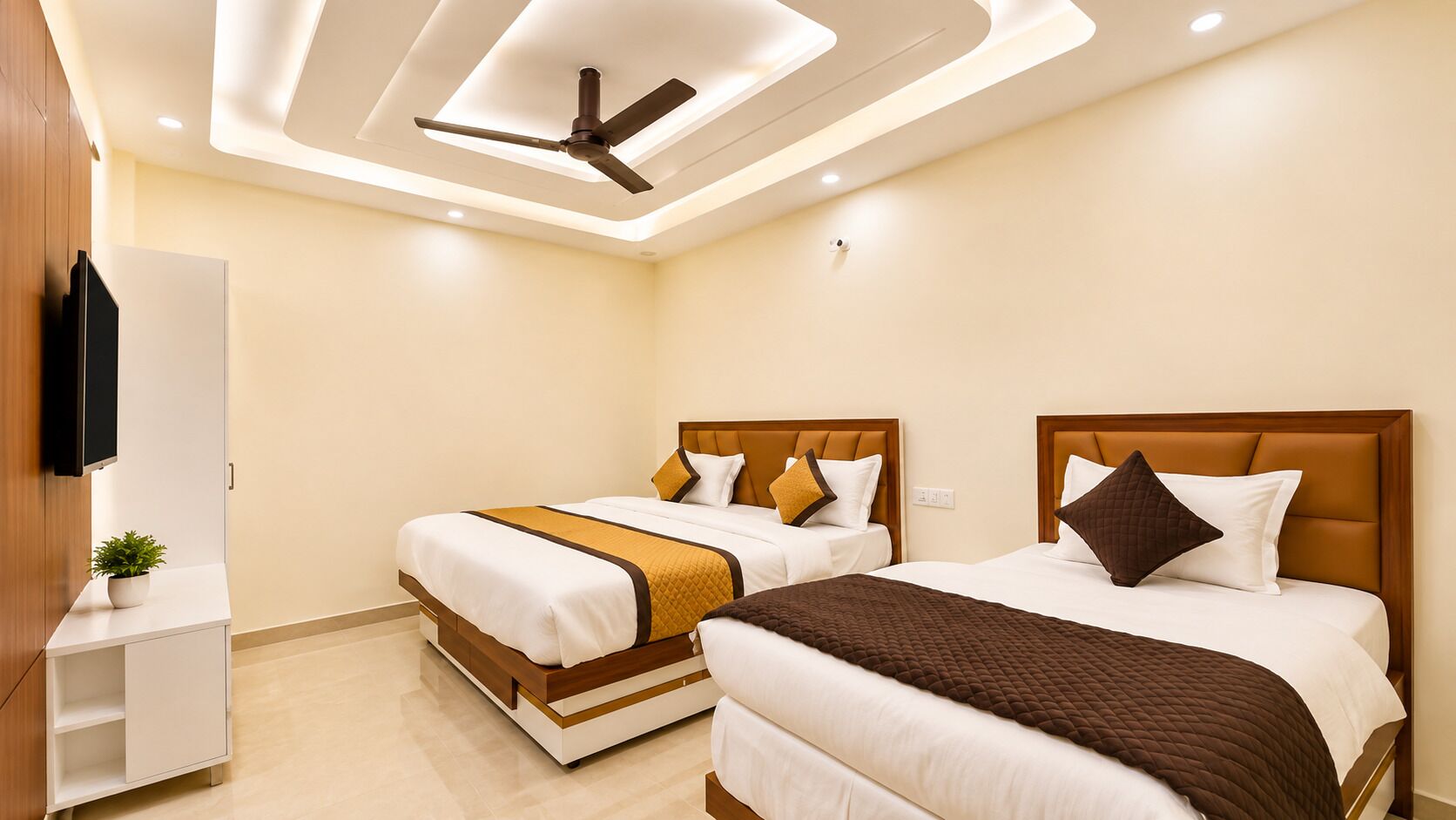 A hotel room with two beds, a ceiling fan, recessed lighting, and a TV mounted on the wall.
