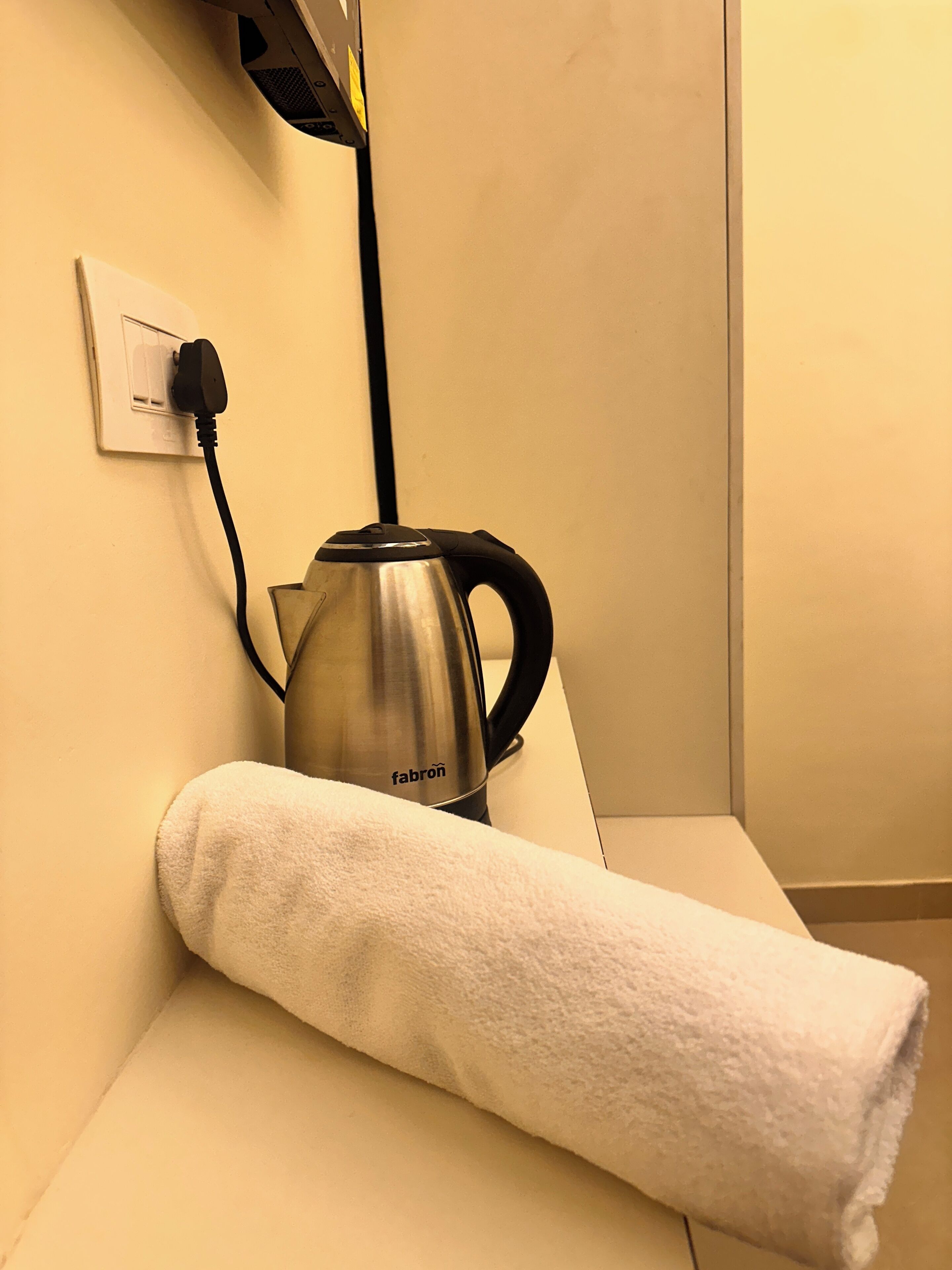 A kettle on a white countertop with a towel rolled up beside it, a power outlet, and a wall socket.