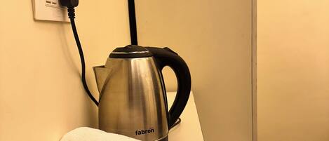 A kettle on a white countertop with a towel rolled up beside it, a power outlet, and a wall socket.