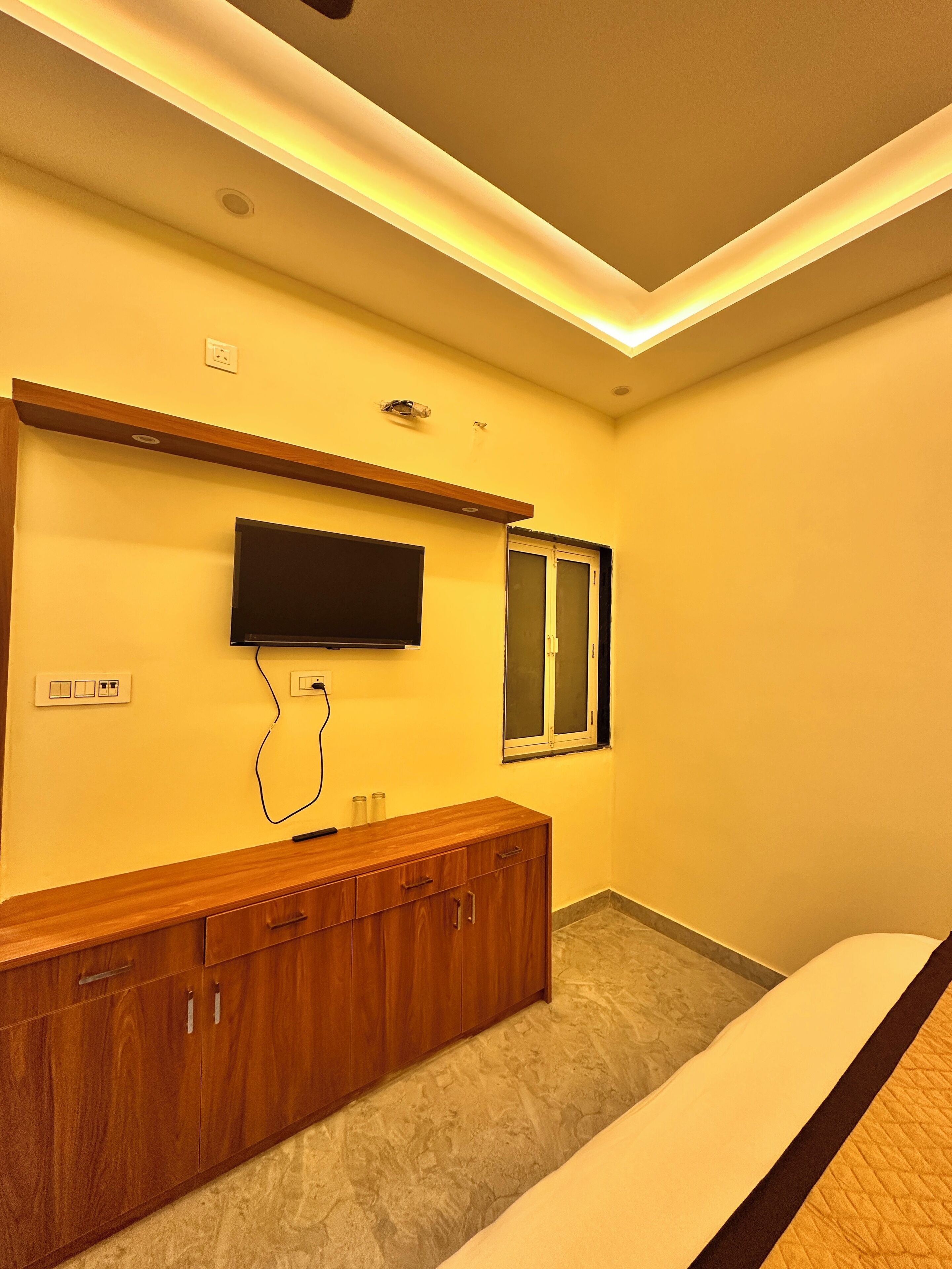 A modern bedroom with a wooden cabinet, a flat-screen TV mounted on the wall, and a window with a view.