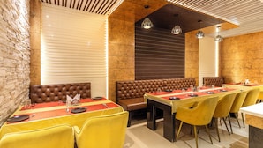 A restaurant with high-backed booths, yellow chairs, and a long communal table with red placemats. - Itsy Hotels Relax (Nagaon)