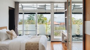 A bedroom with a large bed, a balcony with potted plants, and a view of the outside. - Villa Rumah Kita (Nusa Dua)