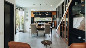 A modern kitchen with a dining area, featuring a large window, pendant lights, and a staircase leading to a loft. - Villa Rumah Kita (Nusa Dua)
