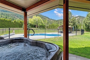 Un bain à remous situé dans un espace extérieur abrité, avec vue sur une piscine et un jardin clos.
