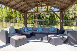 An outdoor patio with a covered seating area, a metal fence, and trees in the background.