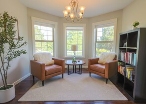 A room with two leather chairs, a small table, a bookshelf, and a large window. - The Tyrolean: Pool, Hot Tub & Ski Hill Charm (Leavenworth)