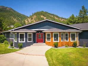 Une maison à deux étages avec une porte d’entrée rouge, un garage et une allée menant à l’entrée.