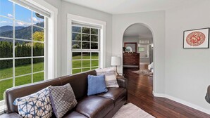 A living room with a leather sofa, patterned cushions, a lamp, and a view of a green landscape through large windows.