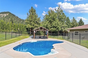 Une piscine agrémentée d’un gazebo en bois, entourée d’une clôture et d’arbres.