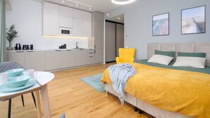 Een moderne hotelkamer met een bed, een bureau met stoel, een kitchenette en kunstwerken aan de muren.
