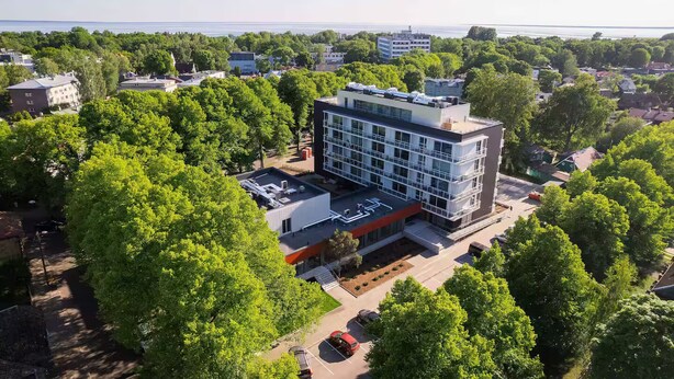 Een modern meerlaags gebouw met een plat dak en grote ramen, omgeven door weelderige groene bomen.