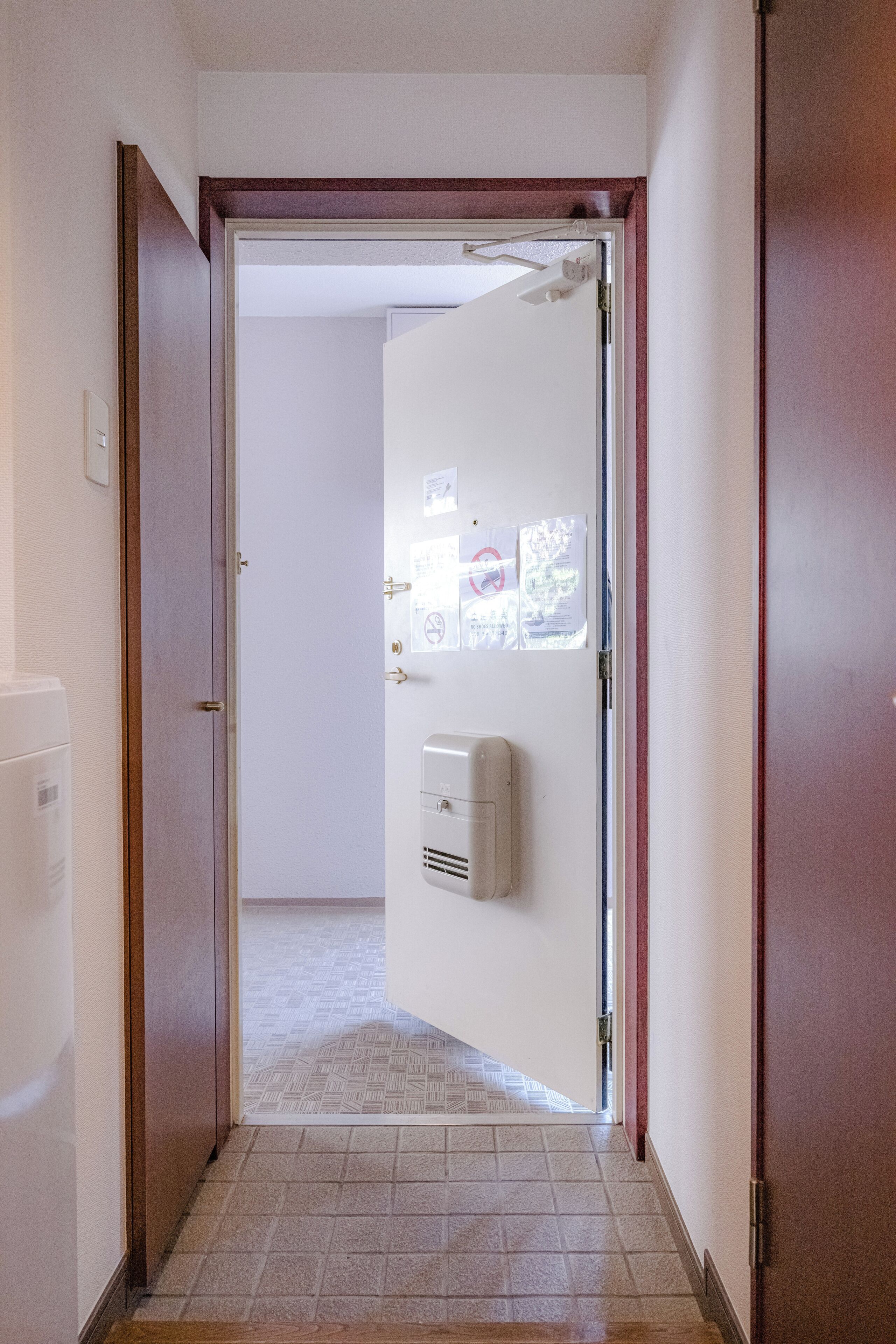 A hallway with a door leading to a room, a hand dryer, and a tiled floor.