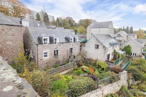 A stone building with a sloped roof, a small garden area with various plants, and a staircase leading to the upper floor. - 4 Bed Main Door House w/ Beautiful River Views (Perth)