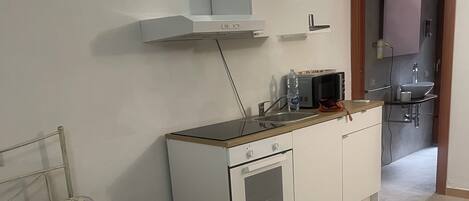 Ein Schlafzimmer mit Bett, einer kleinen Küchenzeile und einem durchgehenden Türspalt sichtbaren Badezimmer.