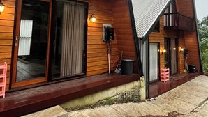 A wooden cabin with a balcony, large windows, and a stone-paved entrance. - Padangsari Cabin House (Dieng Kulon)
