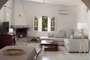 A living room with a fireplace, a sofa, a coffee table, and a television. - Villa Artemis in Small Kounoupi Porto Heli (Porto Cheli)