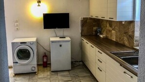 Una cucina funzionale con lavatrice, un piccolo frigorifero, TV a parete e una schiena di marmo.