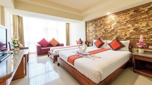 Een hotelkamer met een groot bed, twee kleinere bedden, een televisie, een bureau en een decoratieve wand.