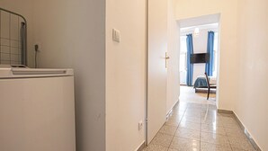 Un pasillo con lavadora, una puerta y una cama con cortinas al fondo.