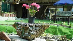 A garden with a decorative planter holding pink flowers, a stone sculpture, and a wooden bench. - The Naturewalk  Riverside Chaffi Bhimtal (Bhimtal)