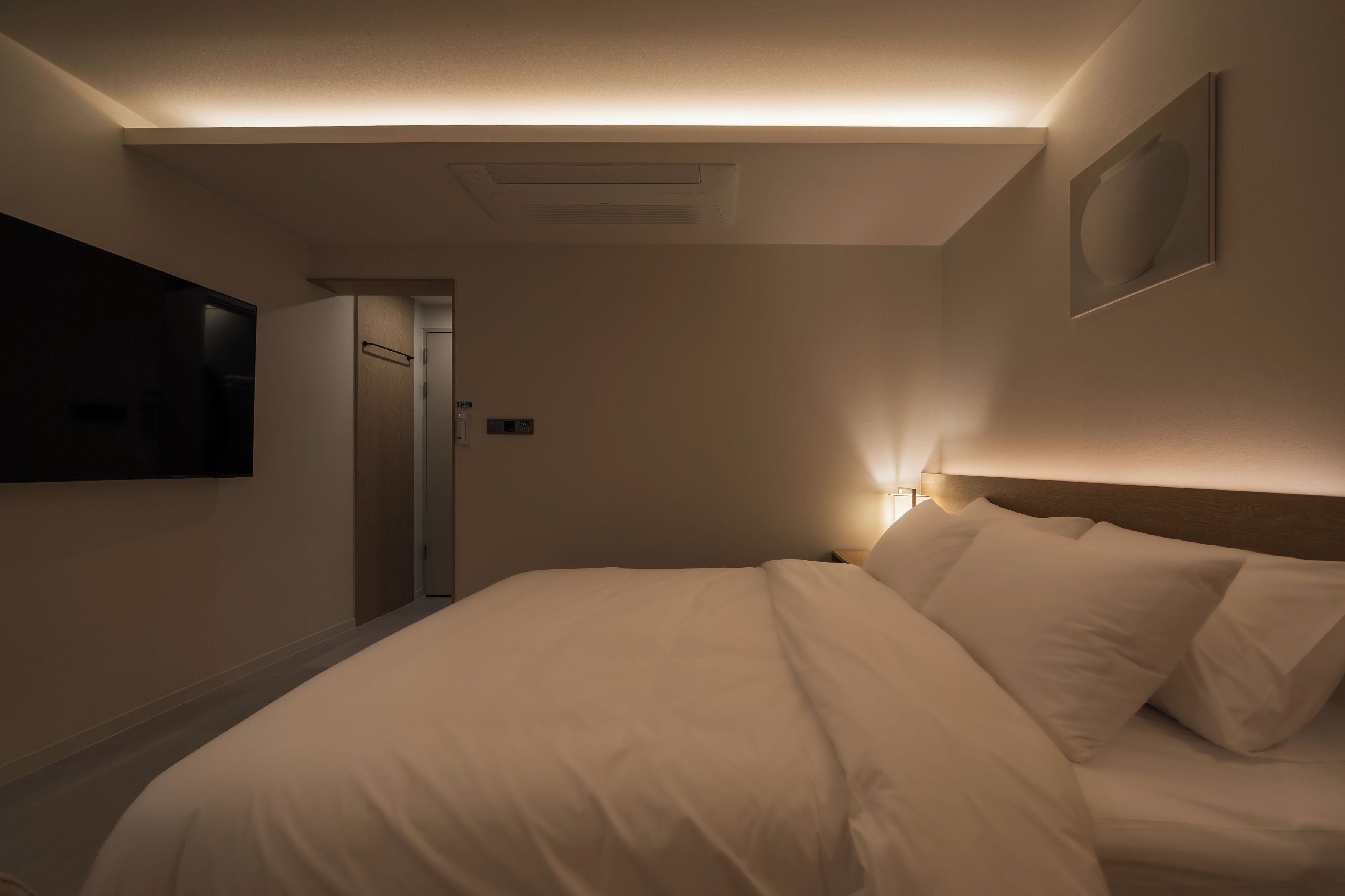 Une chambre d’hôtel avec un lit, un téléviseur fixé au mur et une porte donnant sur une salle de bain.