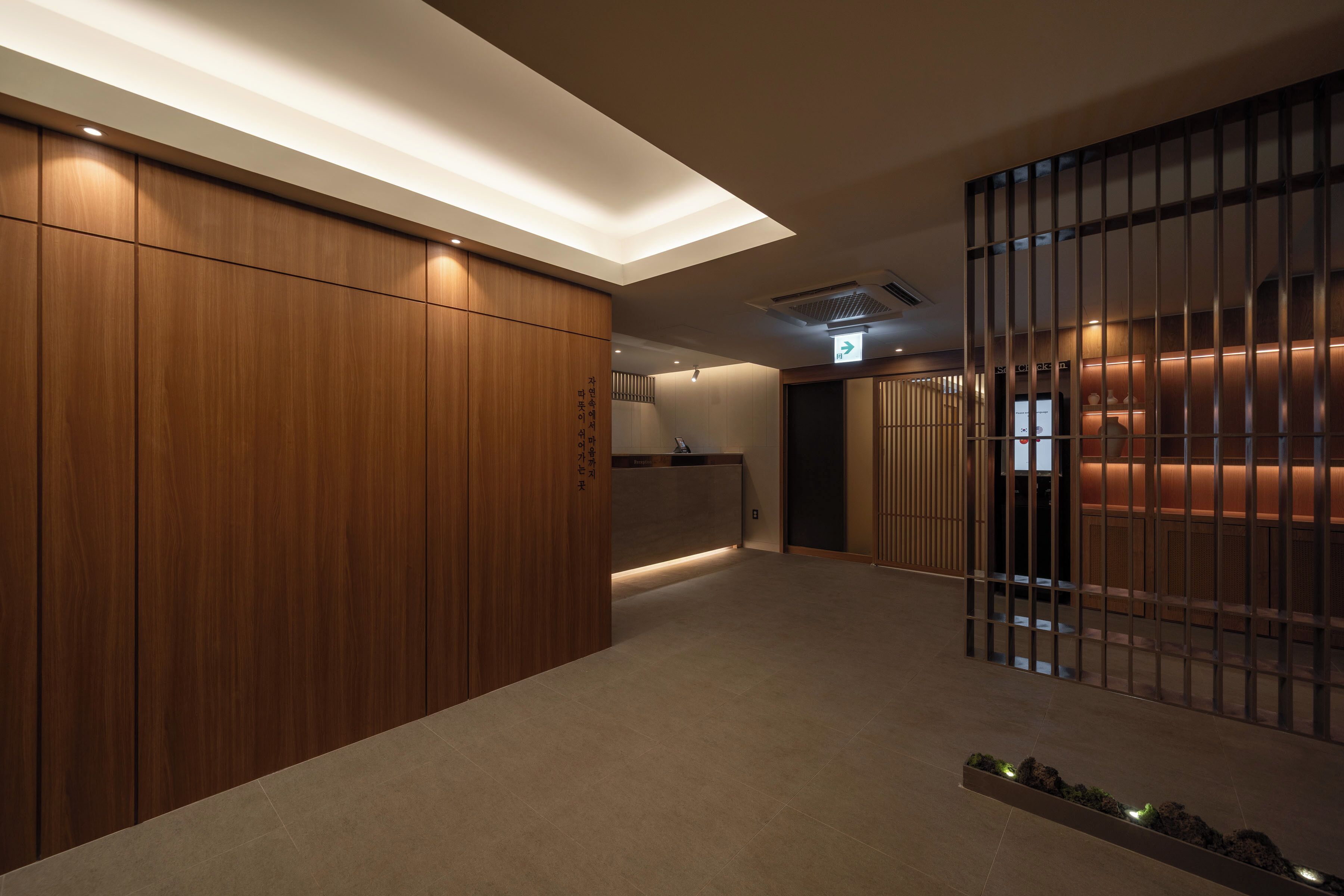 A modern hotel lobby with wooden paneling, a reception desk, and a partition with vertical bars.