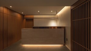 A modern reception area with a wooden reception desk, a reception sign, and a sliding door with vertical slats. - ONSHIMJAE (Pocheon)