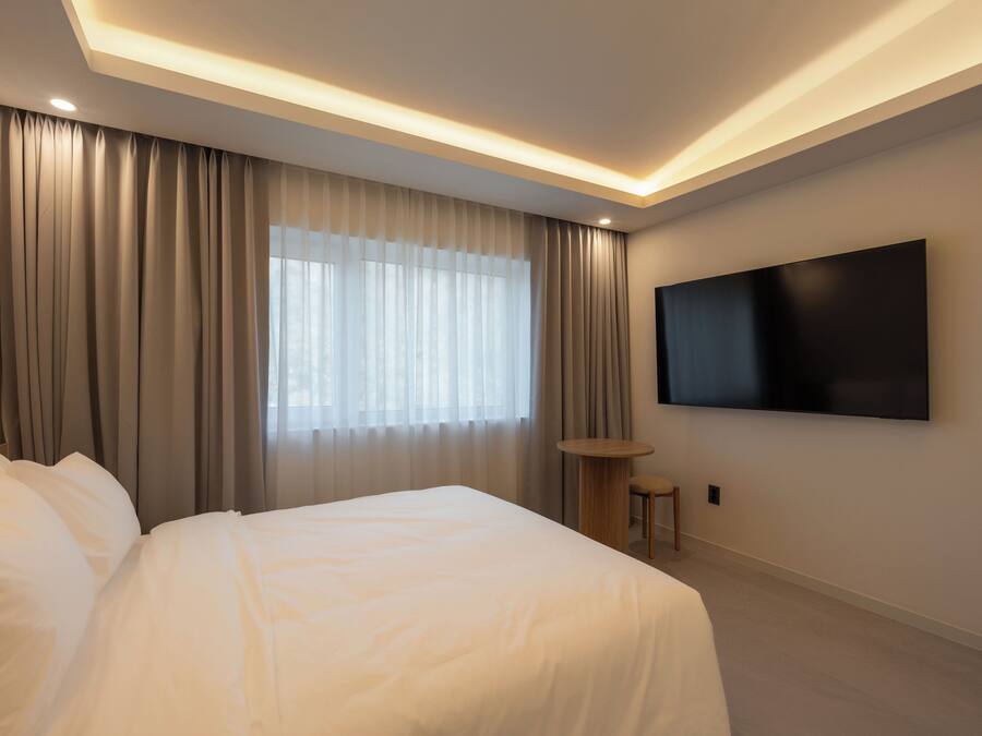 Una habitación de hotel moderna con una cama grande, un televisor de pantalla plana en la pared y un amplio ventanal con cortinas.