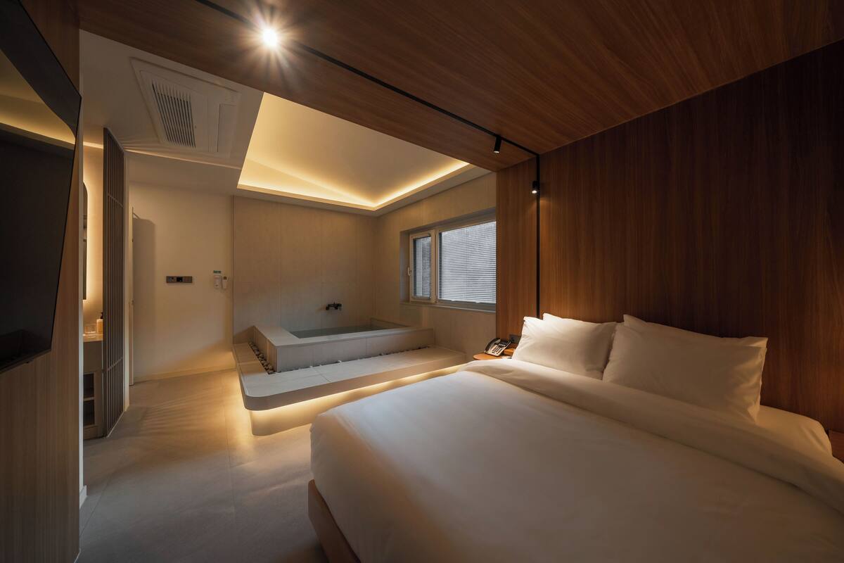 A modern bedroom with a large bed, a built-in bathtub, and a skylight.