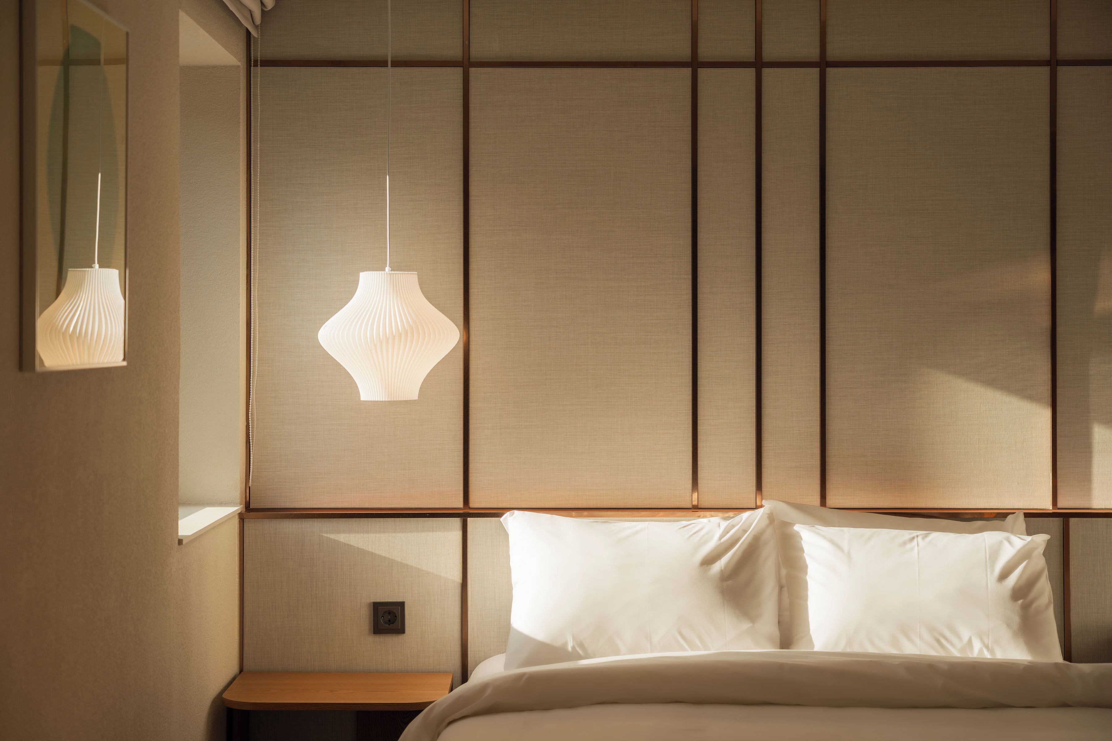 A hotel room with a bed, a nightstand, and two pendant lights.