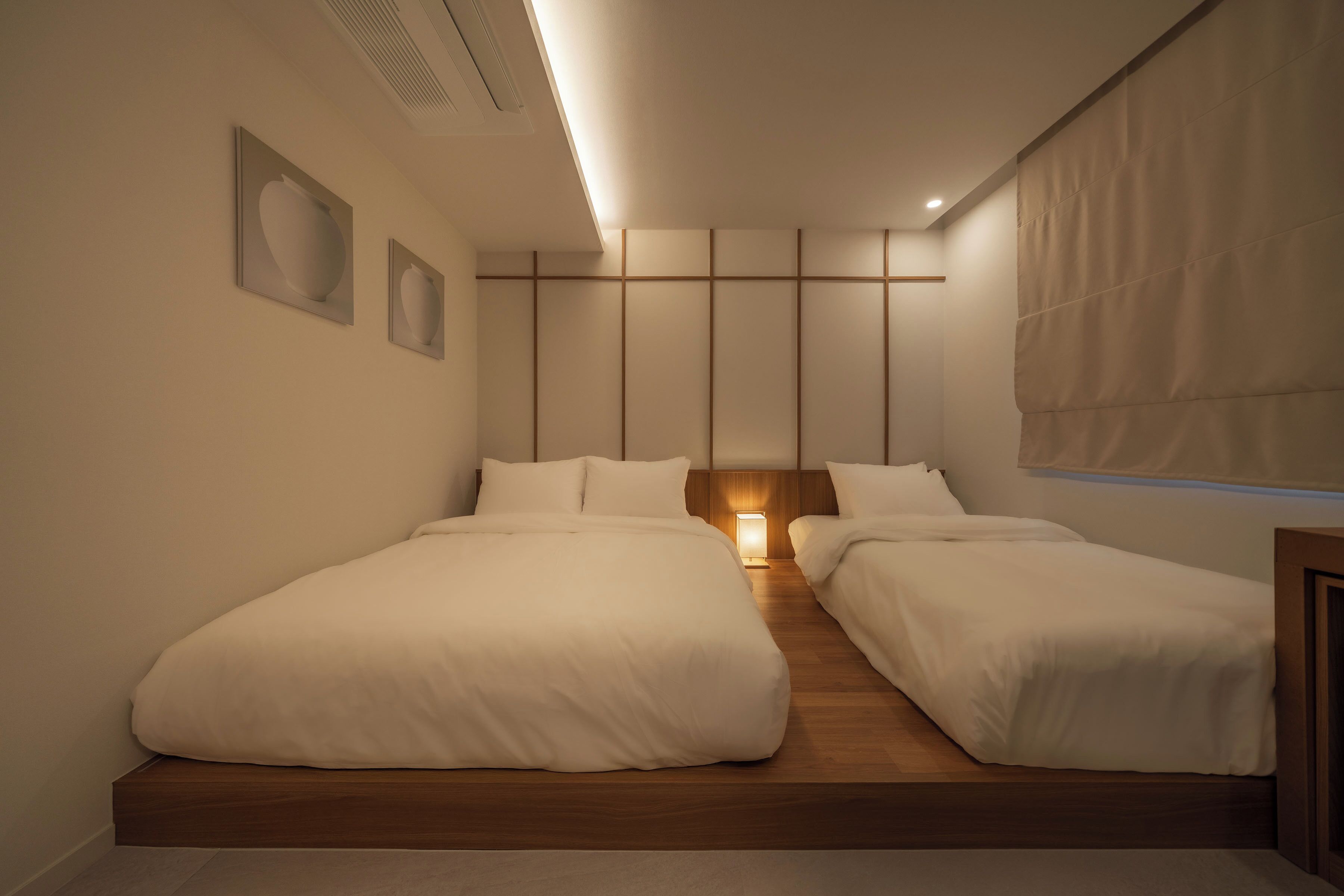 A modern hotel room with two beds, a wooden floor, a nightstand, and a large window with a curtain.